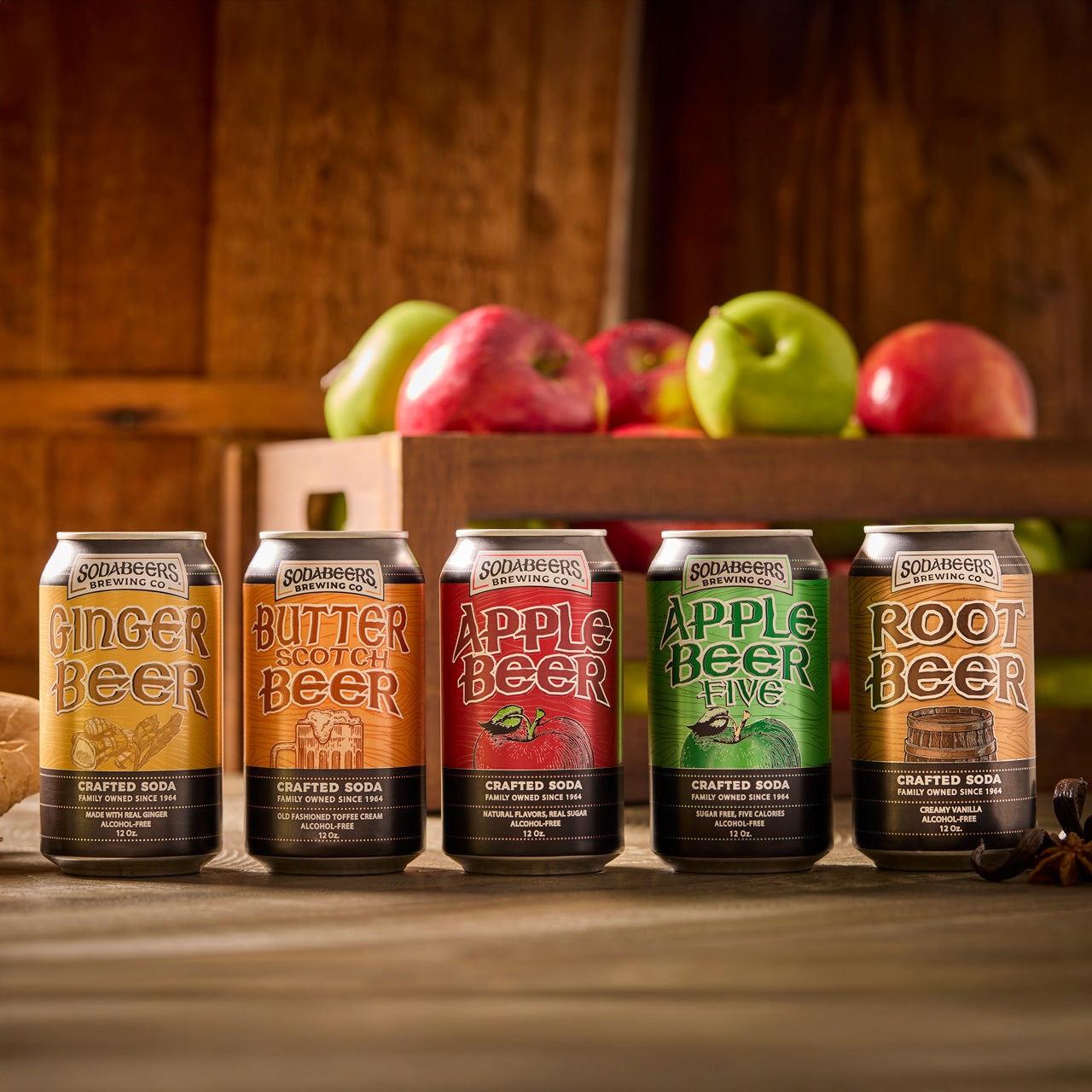 Five cans of SodaBeer Brewing Co. soda with a wooden crate of apples in the background.