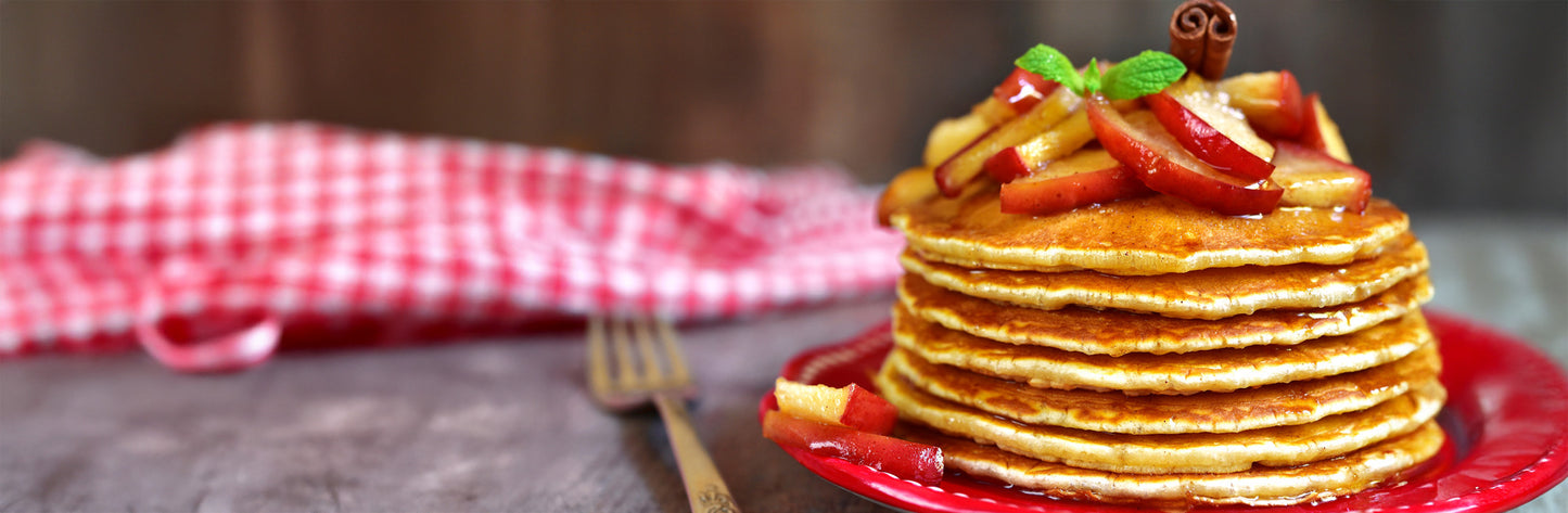 Stack of pancakes with fruit and syrup on a red plate with a blurred background