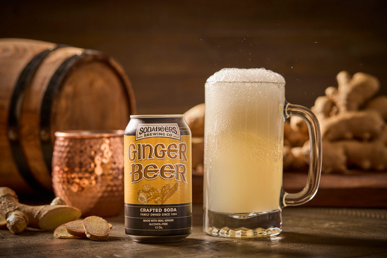 SodaBeers Ginger Beer can with a glass of ginger beer on a wooden surface with ginger and a barrel in the background.