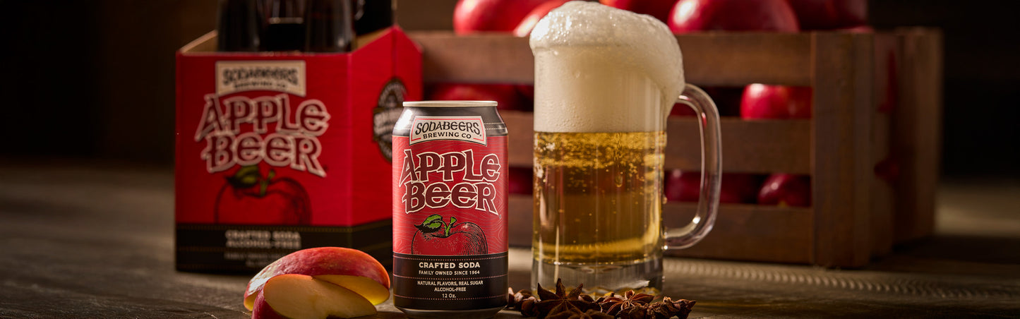 SodaBeers Apple Beer can and bottle with a glass of beer on a wooden surface with apples and a crate in the background.
