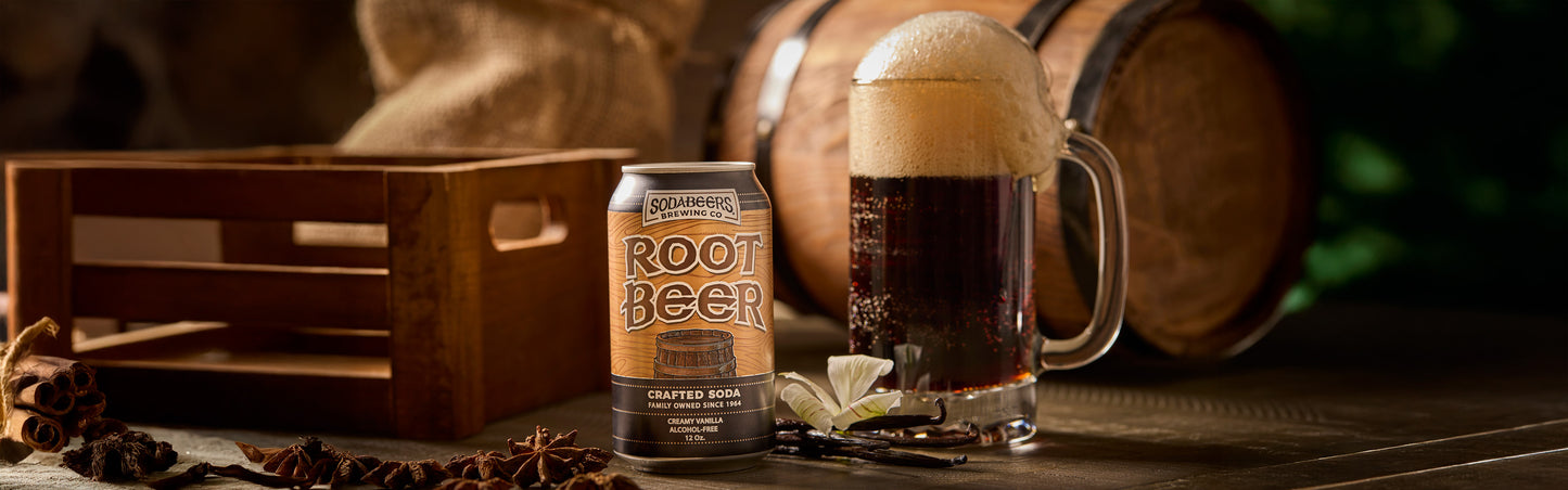 Can of SodaBeers root beer and glass with foam next to wooden crate and barrels on a wooden surface.